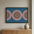 Framed artwork with circular patterns on a wall above a wooden cabinet with a ceramic vase.