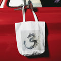 White tote bag with dragon design hanging on a red car door