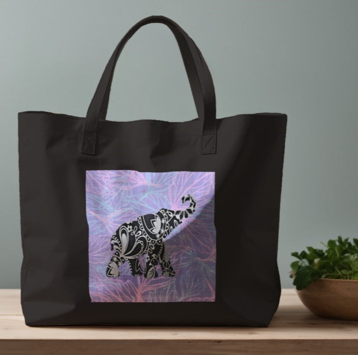 Black tote bag with a decorative elephant design on a wooden surface with a plant in the background.