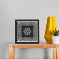 Framed artwork on a wooden table with a yellow lamp and plant in the background