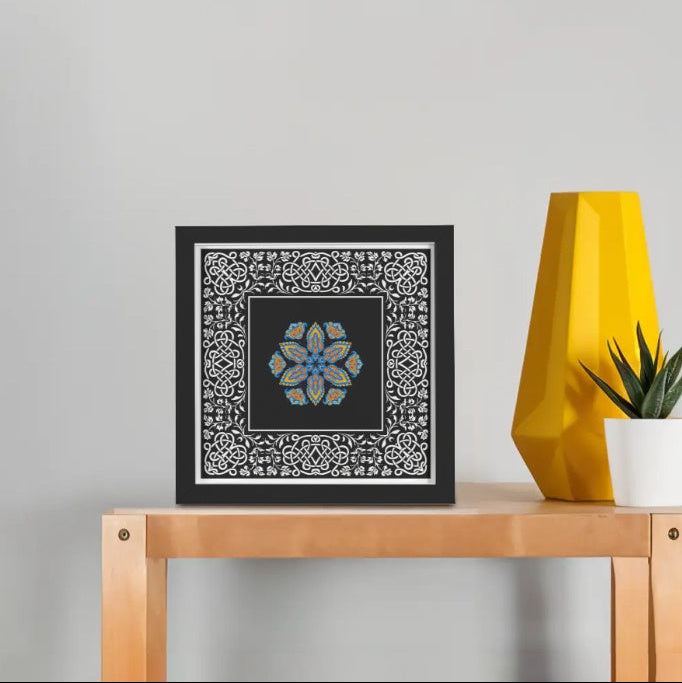 Framed artwork on a wooden table with a yellow lamp and plant in the background