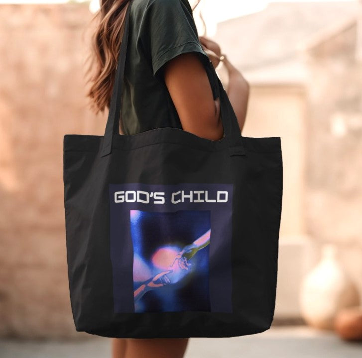 Black tote bag with 'GOD'S CHILD' design held by a person