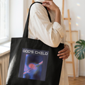 Woman holding a black tote bag with a graphic design and text in a bright room.