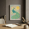 Framed peacock artwork on a wall above a desk with books and a vase.