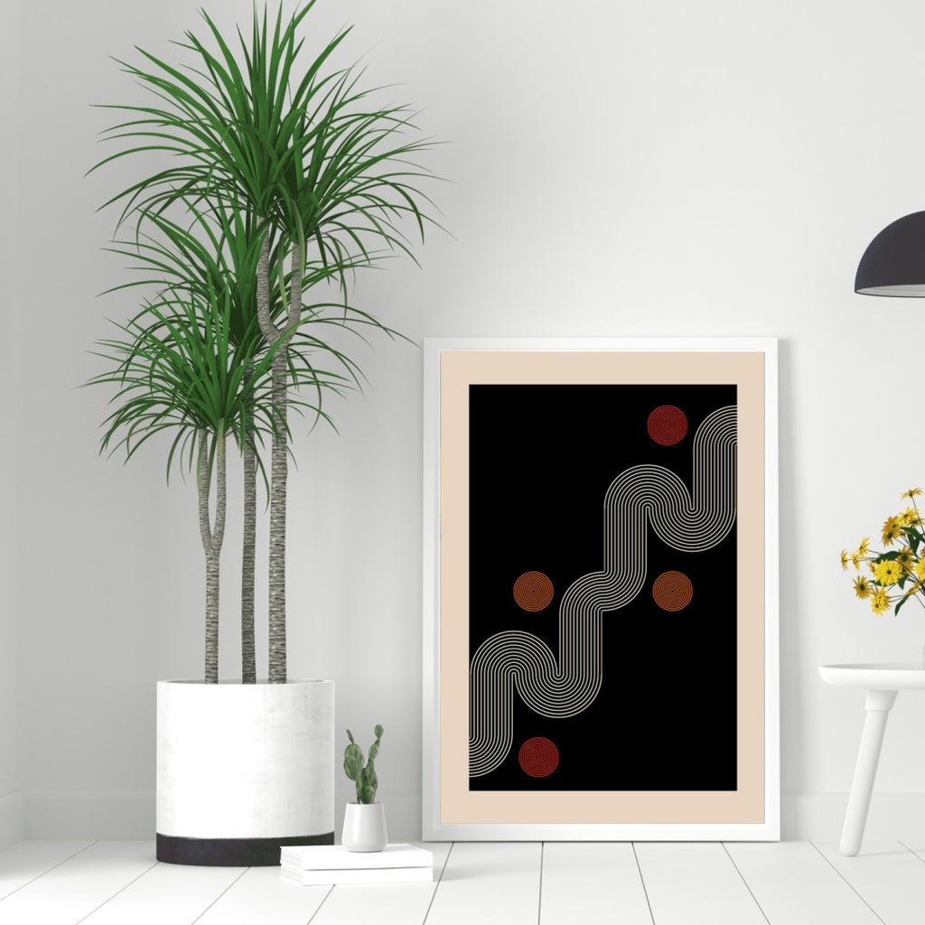 Framed abstract art print on a white wall with a plant and small table in the foreground.